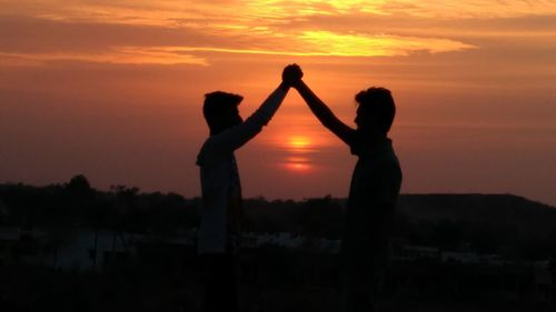 Silhouette people against orange sky during sunset