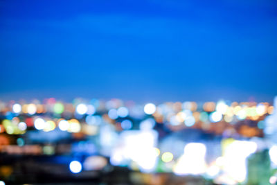 Defocused image of illuminated city against blue sky