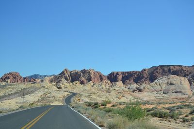 Road leading towards mountains against clear blue sky