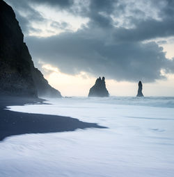 Midday coastal view showcasing rocky formations and crashing waves under moody skies