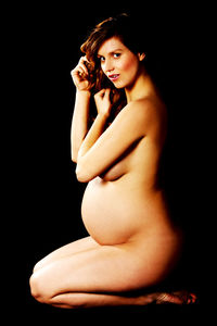Portrait of naked pregnant woman sitting against black background
