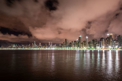 Illuminated city by sea against sky at night