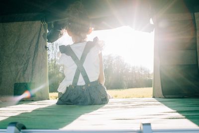 Young girl sat in a tent watching the sun set whilst camping outdoors