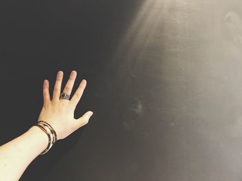 Cropped hand of woman wearing bangles and ring by sunlight in darkroom