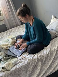 Young woman using mobile phone while sitting on bed at home