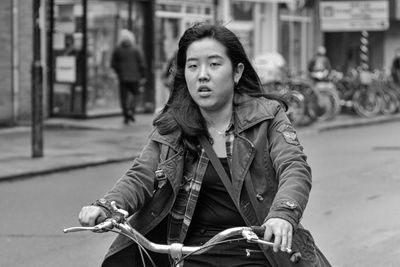 Portrait of young woman with bicycle on street in city