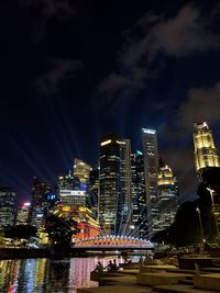 Illuminated buildings by river against sky in city at night