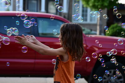 Side view of cute girl playing with bubbles at street