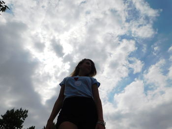 Low angle view of woman standing against cloudy sky