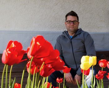 Close-up of tulips blooming against man sitting on bench by wall