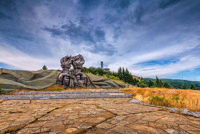 View of cross on landscape against cloudy sky