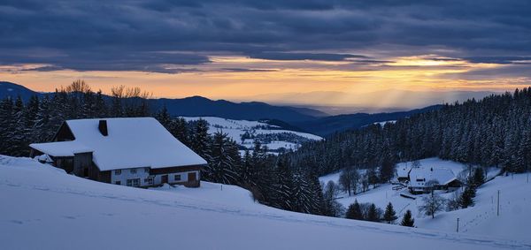 Snow covered houses against sky during sunset