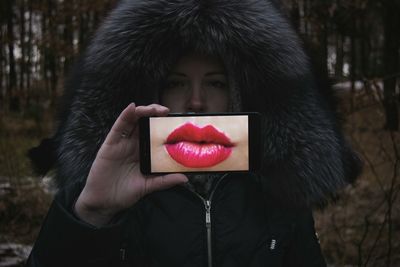 Portrait of young woman holding smart phone showing pink lips in display during winter