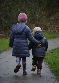 Rear view of siblings walking on pavement in winter