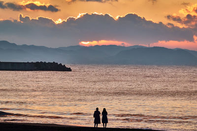 Silhouette people on beach against sky during sunrise