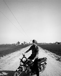 Man wearing turban sitting on motorcycle at field against clear sky