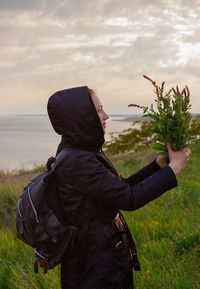 Girl in raincoat  backpack wild flowers. trend local travel recovery concept end of quarantine