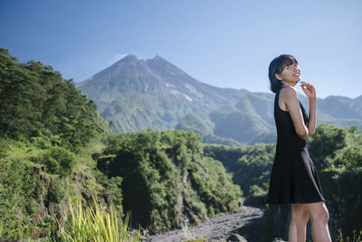 Smiling young woman standing on land against mountains and sky