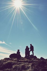 Silhouette people on rock against sky on sunny day