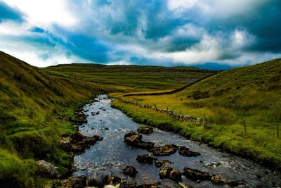 Stream amidst green landscape against sky