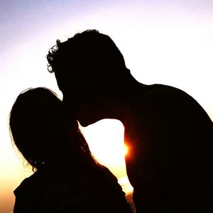 Silhouette man with woman against sky during sunset