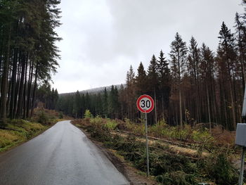 Road sign by trees against sky