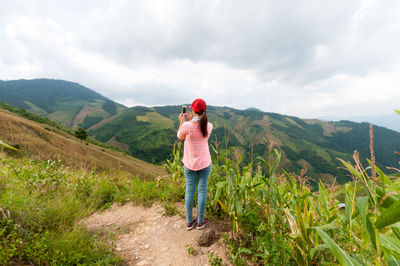 Rear view of woman photographing mountains with mobile phone against cloudy sky