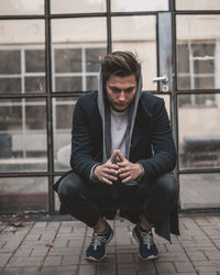 Full length of young man sitting against window