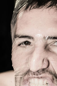 Close-up portrait of man covered in plastic against black background