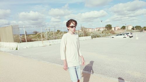 Portrait of young woman standing on road against sky