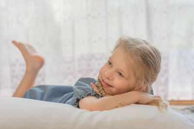 Smiling cute girl looking away while relaxing on bed at home