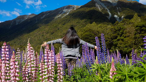 Rear view of woman standing on flowering plants on mountain