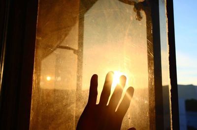 Close-up of hand against sky seen through glass window