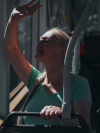 A young blonde woman sits on a tram and waves her hand out the window.