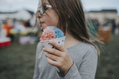 Girl looking away while holding ice candy at field