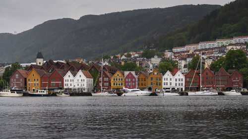 Houses by river and buildings in city against sky