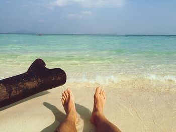 Low section of man relaxing on beach against sky