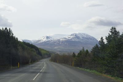 Road amidst trees and mountains against sky