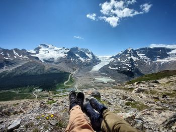 Low section of man sitting on snowcapped mountains against sky