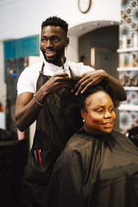 Happy male hairdresser cutting hair of female customer in barber shop