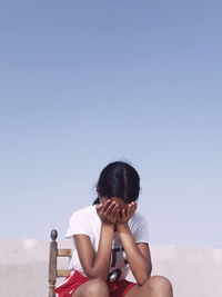 Woman covering face with hands while sitting on chair