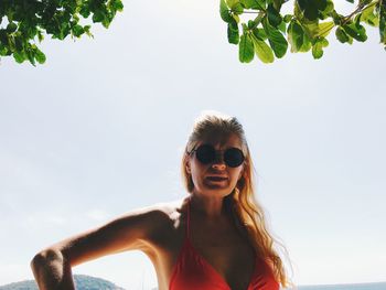Portrait of young woman in sunglasses against sky