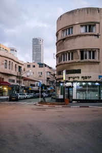 Cars on road by buildings against sky in city