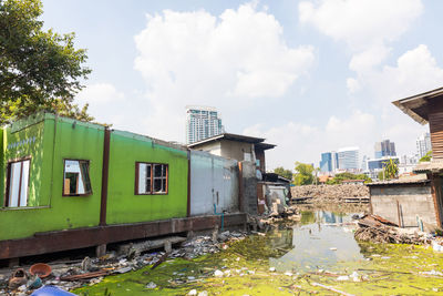 Houses by river against buildings in city against sky