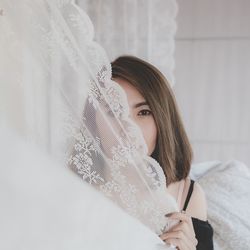 Portrait of woman holding curtain while sitting on bed