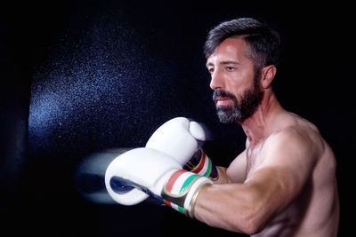 Shirtless male boxer practicing against black background
