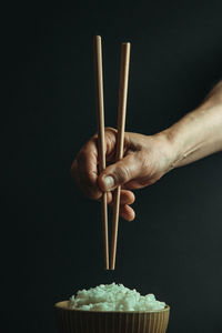 Close-up of hand holding bowl against black background