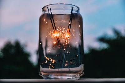 Close-up of sparklers burning in jar on table against sky