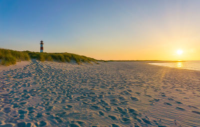 Scenic view of sandy beach against clear sky during sunset