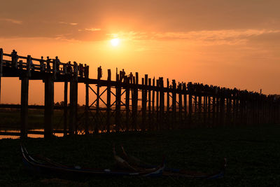 Silhouette wooden posts in sea against sky during sunset